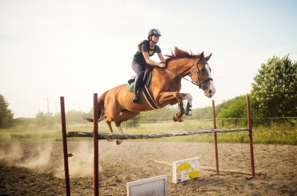 Young female jockey on her horse leaping over hurdle